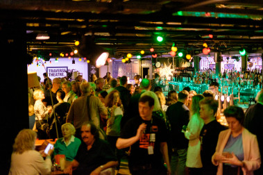 Traverse Bar Café is busy with people. Multi-Coloured lights hand from the ceiling and the square Traverse logo is visible in the background.
