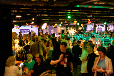 Traverse Bar Café is busy with people. Multi-Coloured lights hand from the ceiling and the square Traverse logo is visible in the background.