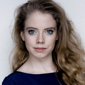 Meghan Tyler has large blue eyes and long, loosely curled blonde hair.
