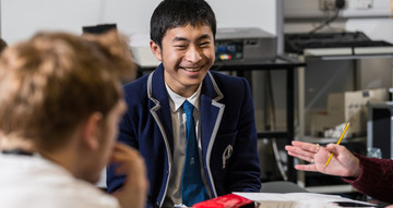 A teenage boy in a smart blue blazer smiles at the camera.