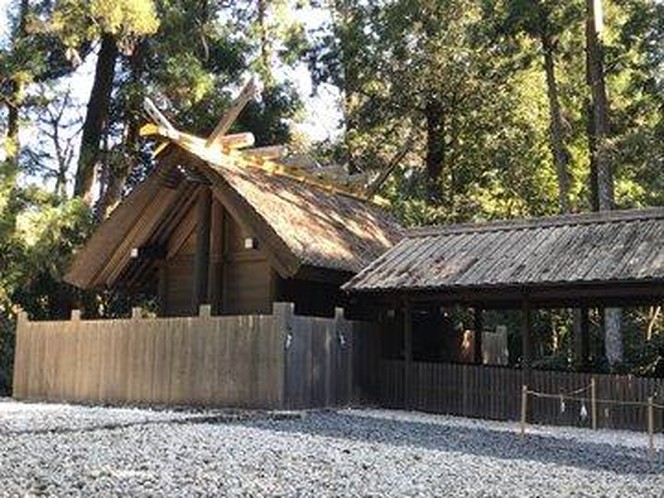 A traditional wooden hut-style shrine underneath a canopy of trees in the sunlight.